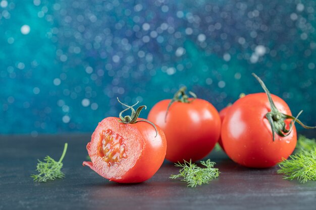 Drie verse tomaten met bladeren op een donkere ondergrond.