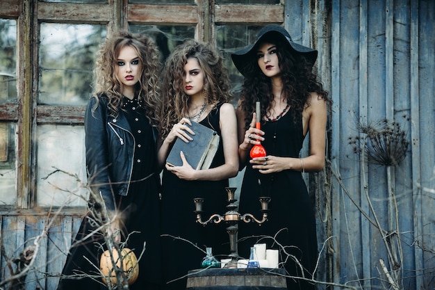 Drie vintage vrouwen als heksen poseren bij een verlaten gebouw aan de vooravond van halloween