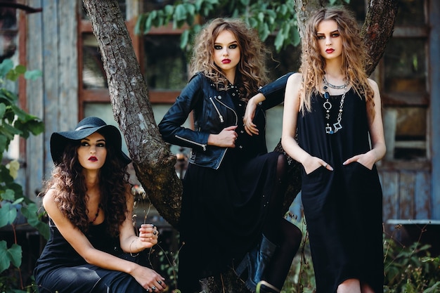 Drie vintage vrouwen als heksen poseren voor een verlaten gebouw aan de vooravond van Halloween