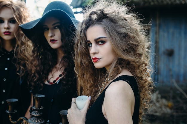 Drie vintage vrouwen als heksen poseren voor een verlaten gebouw aan de vooravond van halloween