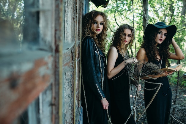 Drie vintage vrouwen als heksen poseren voor een verlaten gebouw met boeken in de hand aan de vooravond van Halloween