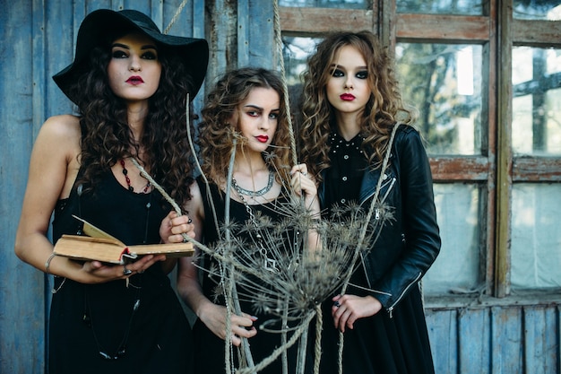 Gratis foto drie vintage vrouwen als heksen poseren voor een verlaten gebouw met boeken in de hand aan de vooravond van halloween