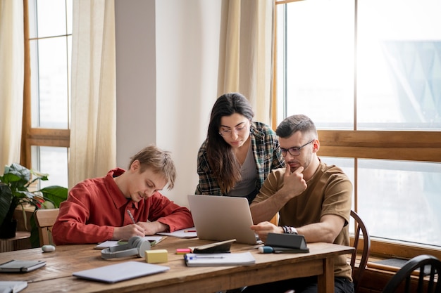 Drie vrienden die boeken en een laptop gebruiken om in een bibliotheek te studeren