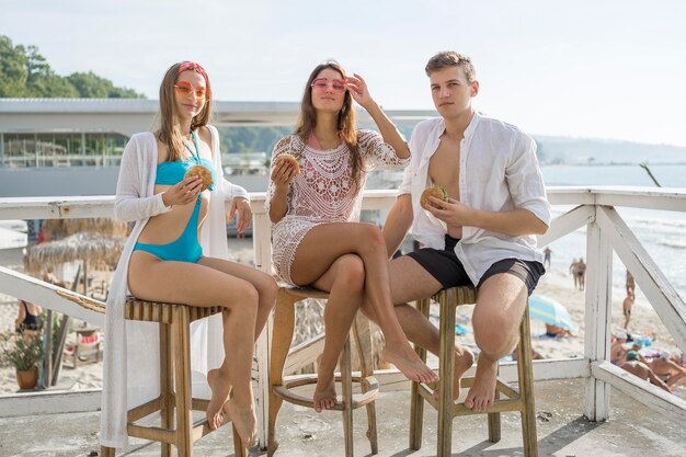 Drie vrienden die samen genieten van hamburgers op het strand