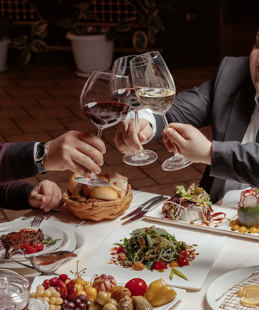 Drie vrienden juichen wijnglazen met rode en witte wijn toe tijdens het diner