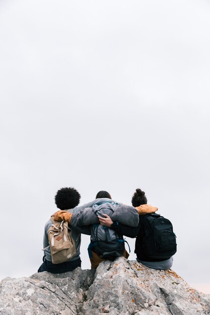 Drie vrienden met hun armen rond zitten op de top van de berg