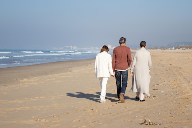 Drie vrienden van middelbare leeftijd die een zonnige herfstdag samen doorbrengen terwijl ze langs de kust wandelen. Senior paar en kortharige dame genieten van vrije tijd samen. Vrienden, vrijetijdsconcept