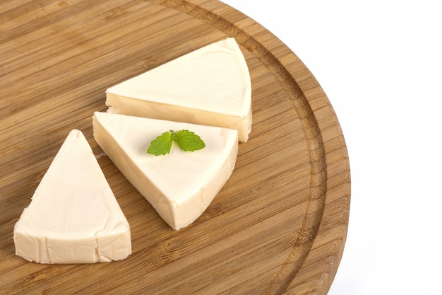 Driehoek roomkaas stukjes met munt op een houten bord geïsoleerd op een witte tafel