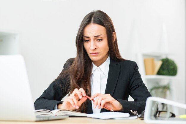 Droevige jonge onderneemster die rood potlood in haar handzitting bij bureau houdt