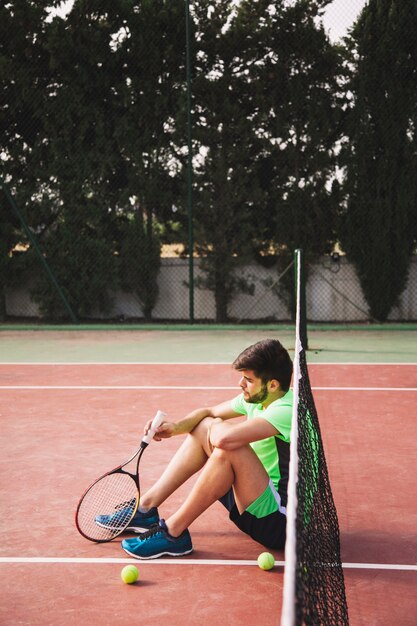 Droevige tennisspeler leunend tegen netto