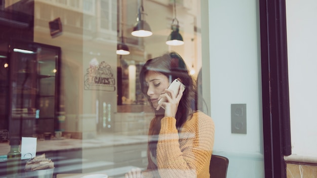 Droevige vrouw die op telefoon in koffie spreekt