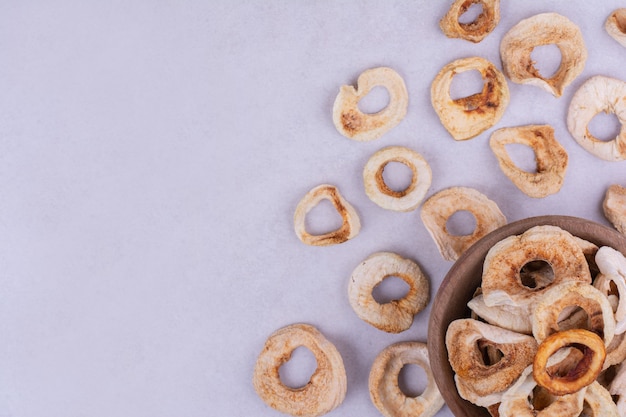 Droge appelschijfjes in een houten beker op grijs.