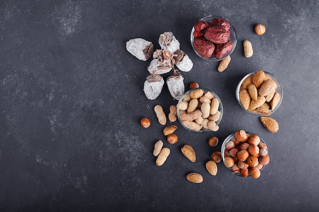 Droge noten en fruit in een glas en houten kopjes op grijze ondergrond, bovenaanzicht.