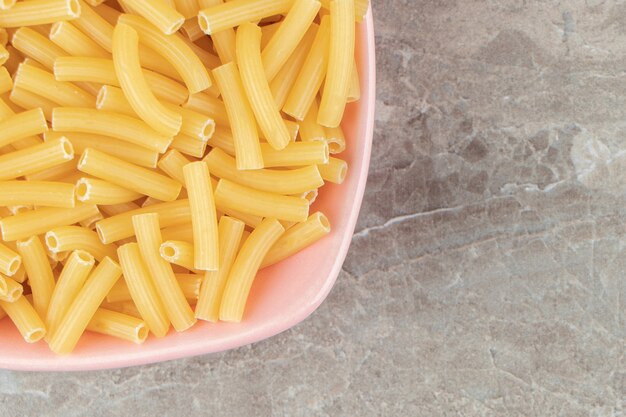 Droge pasta in de vorm van smalle buisjes in roze kom