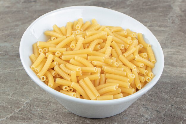 Droge pasta in de vorm van smalle buisjes in witte kom