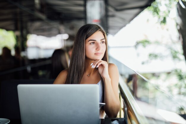 Dromen mooie student meisje zit in het moderne zomerterras café met haar computer