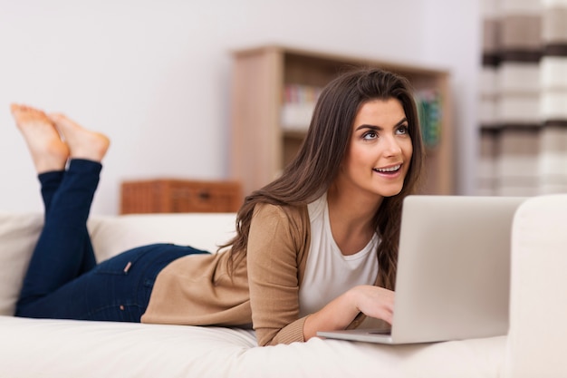 Dromende vrouw die laptop op bank met behulp van