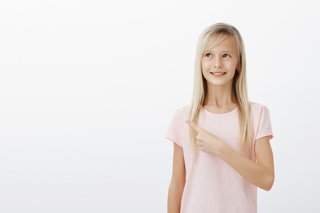 Dromerig schattig blond meisje wijzend naar de linkerbovenhoek tevreden, beeldvormend of denkend