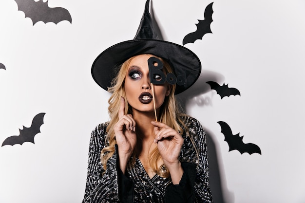 Dromerige blonde vrouw die zich voordeed op halloween-feest. Binnenfoto van elegant vampiermeisje dat van Carnaval geniet.