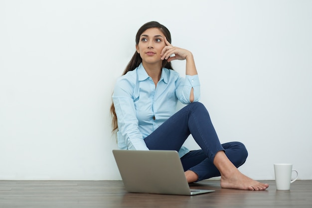 Dromerige jonge vrouw met laptop en thee op Vloer