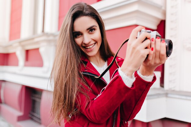 Dromerige vrouwelijke fotograaf met trendy manicure buiten werken en lachen