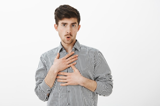 Dronken grappige blanke mannelijke collega in gestreept shirt, gek maken met domme collega, lippen vouwen en zichzelf aanraken, handen vasthouden op de borst, speels en ongericht zijn over grijze muur