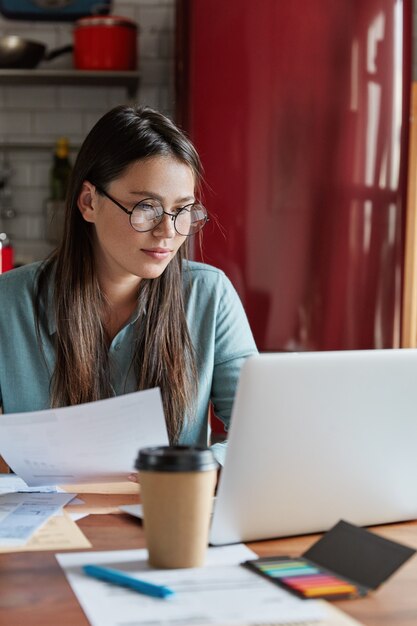 Drukke financier controleert rekeningen van papieren, gericht op het scherm van de laptop