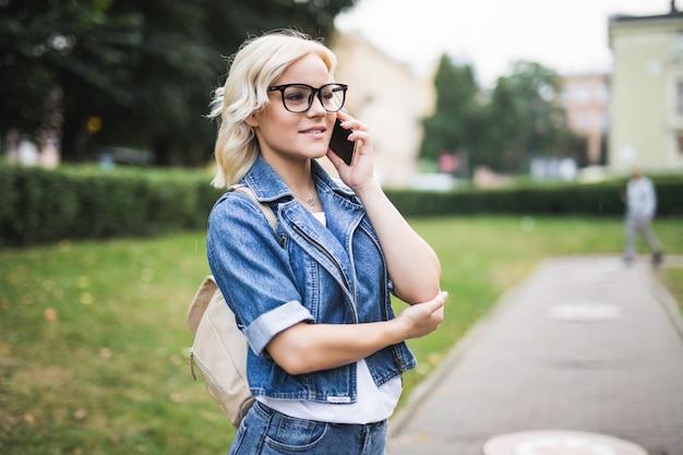 Drukke jonge blonde vrouw meisje gebruikt telefoon om te bladeren door sociaal netwerk gesprek in de stad herfst vierkante ochtend