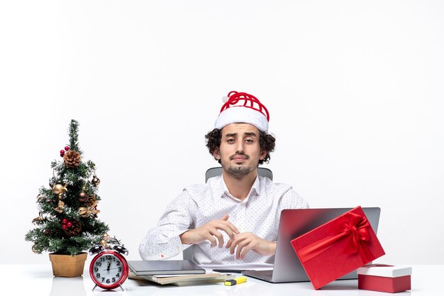 Drukke jonge zakenman met grappige kerstman hoed poseren voor camera in het kantoor op witte achtergrond