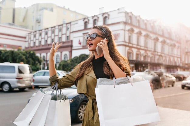 Drukke shopaholic vrouw met tassen praten over de telefoon en wachten op bus in de stad