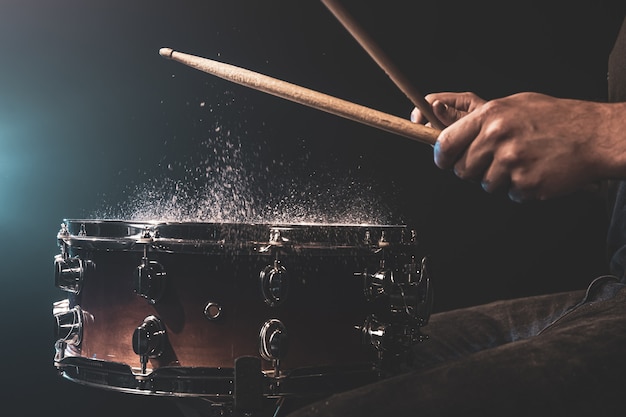 Drummer met drumstokken die snare drum raken met opspattend water op zwarte achtergrond onder studioverlichting close-up.