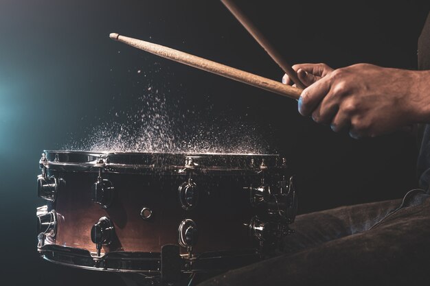 Drummer met drumstokken die snare drum raken met opspattend water op zwarte achtergrond onder studioverlichting close-up.