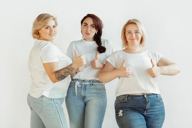 Duimen omhoog. jonge blanke vrouwen in vrijetijdskleding die samen plezier hebben. vrienden die zich voordeed op een witte achtergrond, lachend, ziet er gelukkig en goed onderhouden uit. lichamelijk positief, feminisme, van zichzelf houden, schoonheidsconcept.