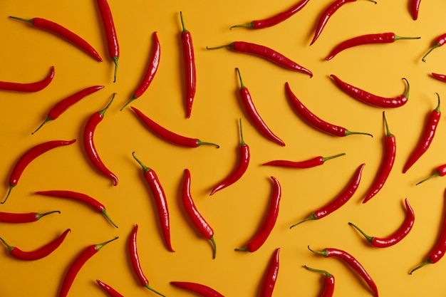 Dunne lange rode chilipeper op gele achtergrond voor het maken van kruiden, sauzen of gerechten. Mix van verse hete groente voor het verbranden van vetten, afvallen en gezonde voeding. Voedsel en ingrediënten concept