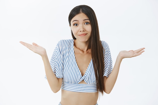 Dwaze, onbewuste schattige vriendin met donker haar in bijgesneden stijlvolle blouse schouderophalend palm omhoog