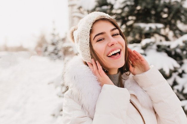 Echte heldere emoties van winter vrouw in gebreide muts glimlachend op straat vol met sneeuw.