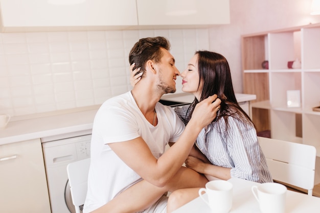 Echtpaar kussen tijdens het ontbijt in witte gezellige kamer