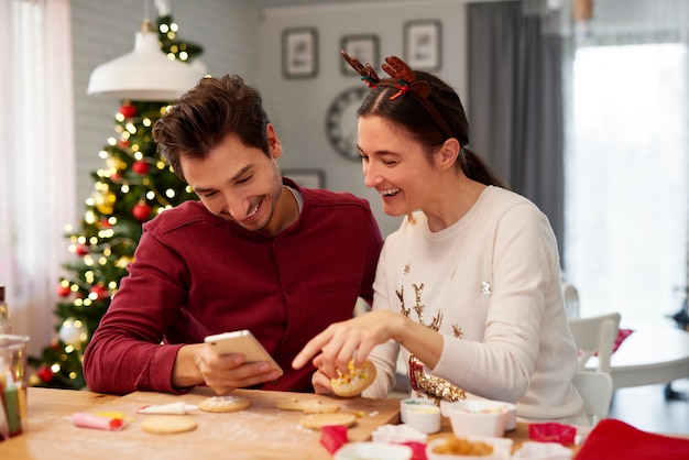 Echtpaar met mobiele telefoon kerstkoekjes versieren