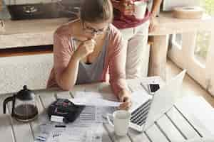 Gratis foto echtpaar met schuldenproblemen, niet in staat hun hypotheek af te lossen. nadenkende vrouw die gefrustreerd kijkt, pen houdt terwijl het beheren van gezinsbudget, berekeningen maakt gebruikend calculator en notitieboekjepc