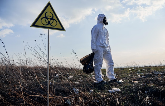 Ecoloog staat in het veld met vuilnis en biologisch gevarenbord