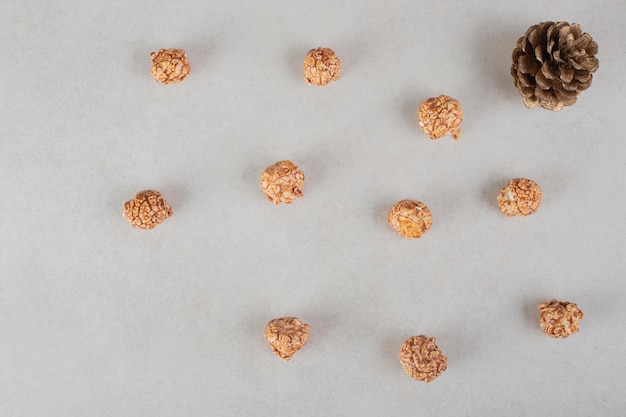 Gratis foto een aantal gekonfijte stukjes popcorn naast een dennenappel op een marmeren ondergrond.