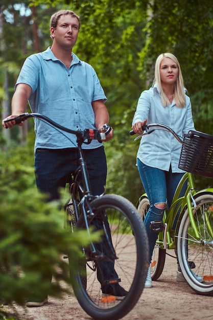 Gratis foto een aantrekkelijk stel van een blonde vrouw en man gekleed in casual kleding op een fietstocht in een park.