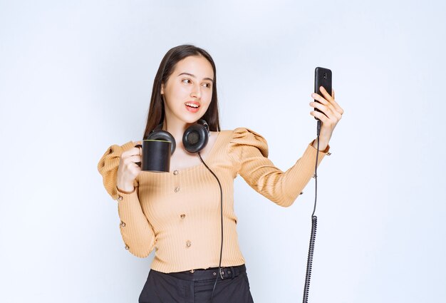 Een aantrekkelijk vrouwenmodel dat selfie neemt met een kopje drank en een koptelefoon.