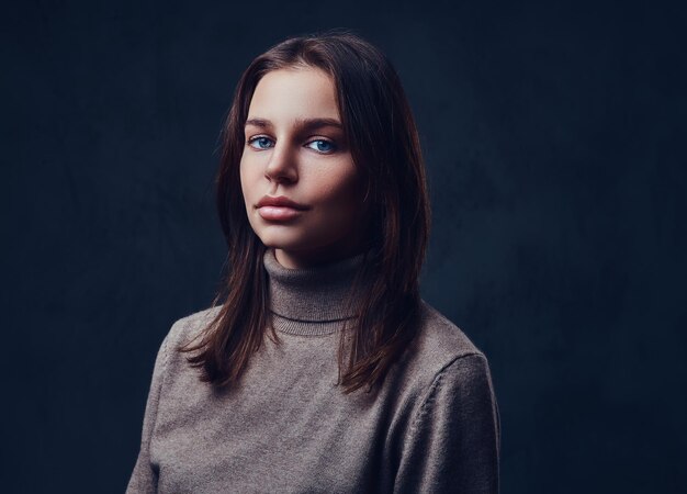 Een aantrekkelijke brunette vrouw gekleed in een bruine jas met lange nek over grijze achtergrond.