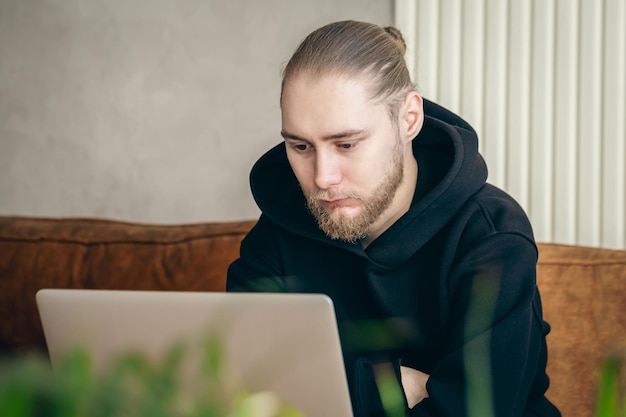 Een aantrekkelijke jonge man met een baard werkt op een laptop