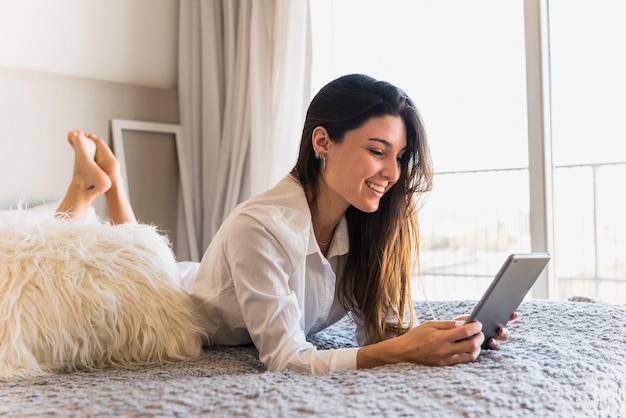 Gratis foto een aantrekkelijke jonge vrouw die op bed ligt dat digitale tablet gebruikt