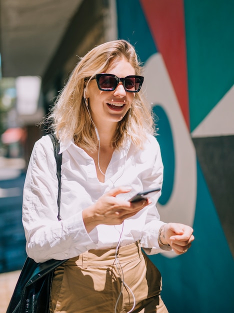Een aantrekkelijke jonge vrouw die zonnebril draagt die cellphone in zonlicht gebruikt