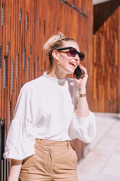 Een aantrekkelijke jonge vrouw die zonnebril draagt die terwijl het nemen van cellphone glimlacht