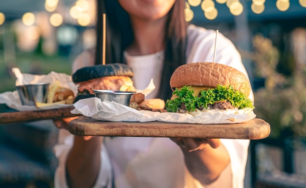 Gratis foto een aantrekkelijke jonge vrouw in handen houdt twee hamburgers op een onscherpe achtergrond