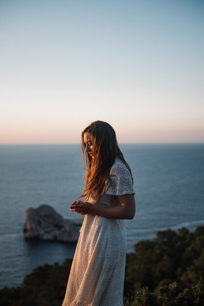 Een aantrekkelijke jonge vrouw met een mooie witte jurk die 's avonds langs de zee loopt